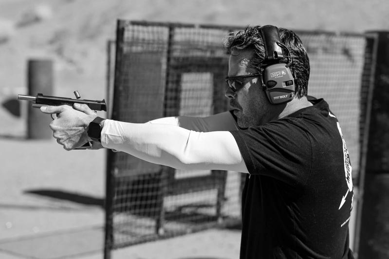 Ballistic team member firing a pistol on a desert shooting range as a spent casing ejects
