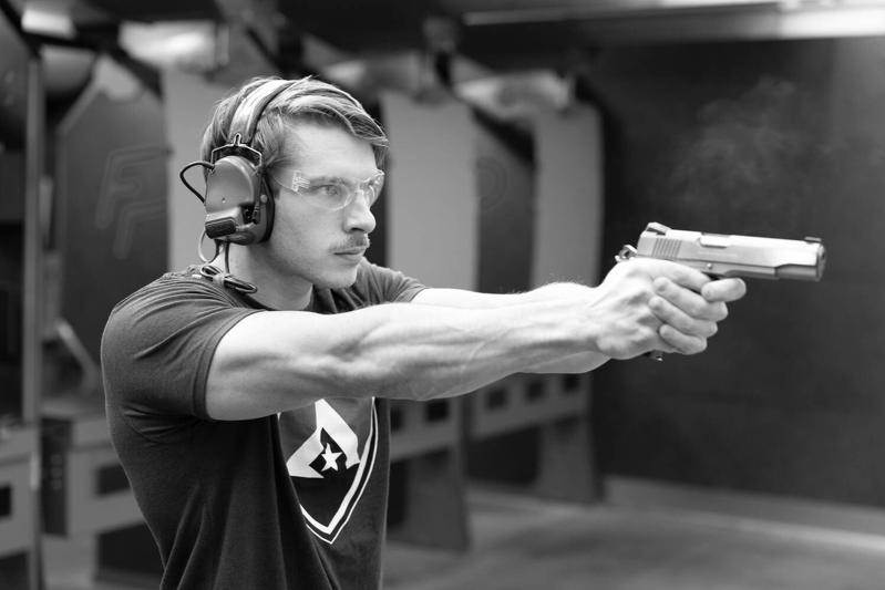 Ballistic team member in hearing protection and safety glasses firing a 1911 pistol at an indoor range