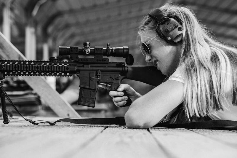 Ballistic team member shooting a scoped rifle from a bench at an outdoor range